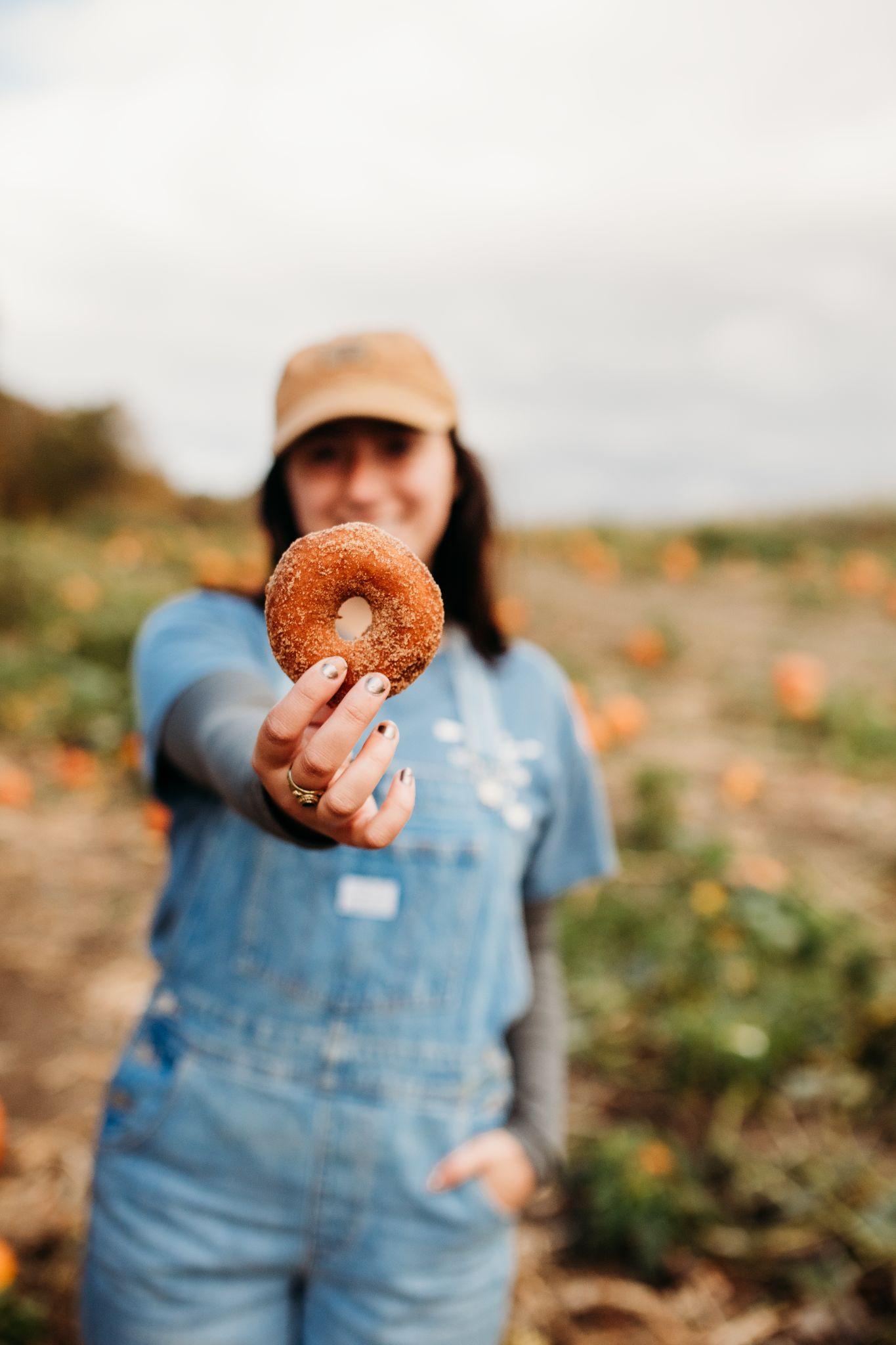 A fresh apple cider donut held up in the pumpkin patch