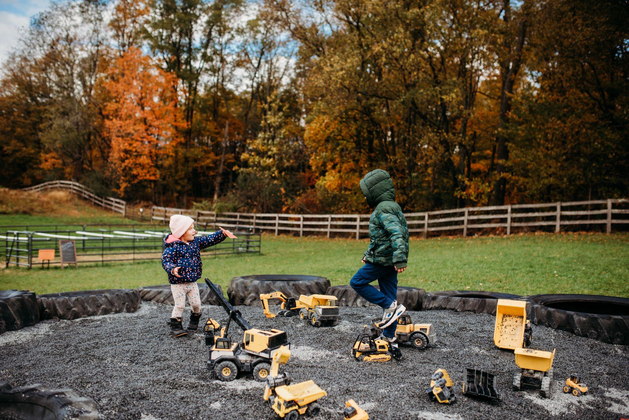 Two kids playing with toy trucks in the pea gravel pit